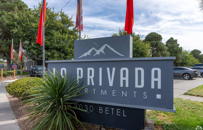 A sign for Privada Artments stands in front of a tree.