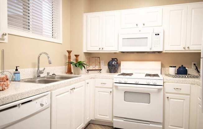 A white kitchen with a stove, sink, and cabinets.