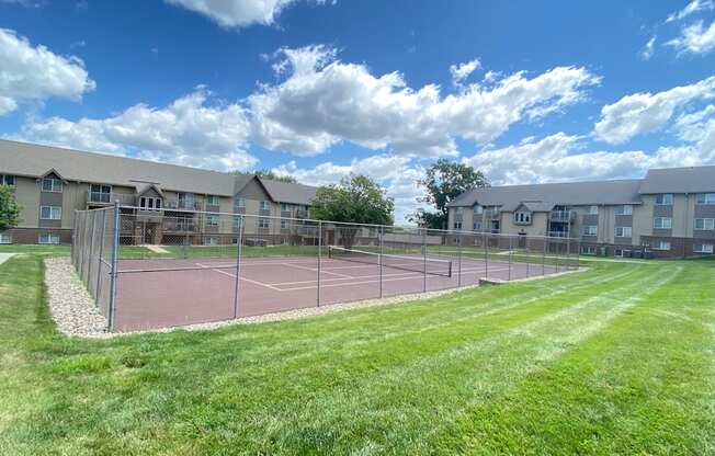 The tennis court at Olde English Village, surrounded by well-kept grounds and nearby apartment buildings.