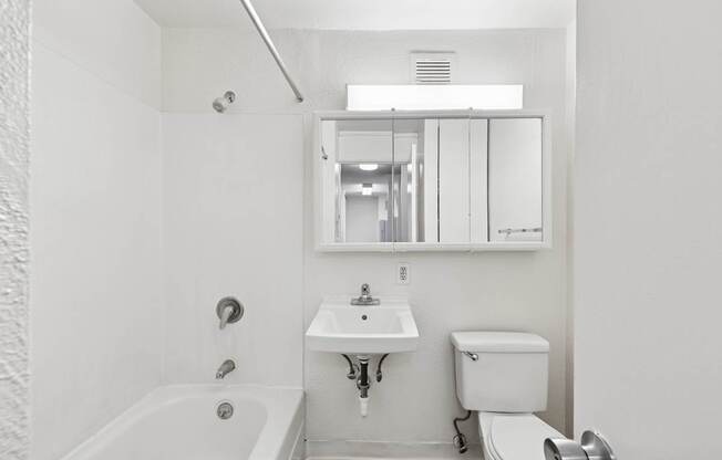 A white bathroom with a tub, sink, toilet and mirror.