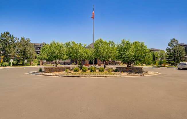 a parking lot with a flag pole and a roundabout with trees and a building at The Fletcher Southlands, Aurora, CO
