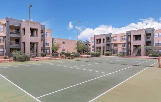 A tennis court is surrounded by apartment buildings.