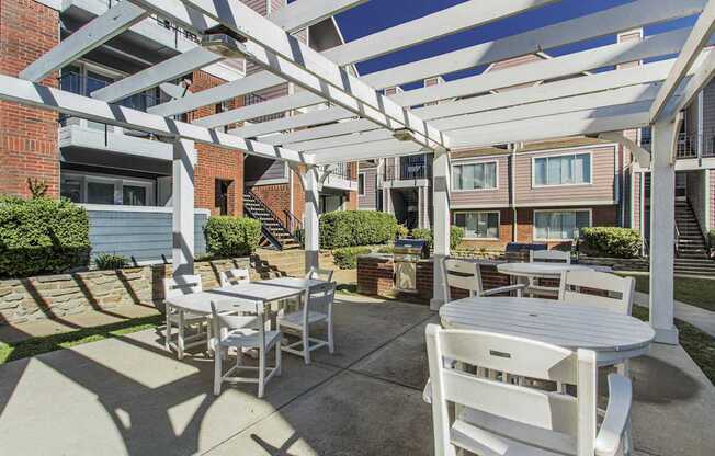 A white patio with a table and chairs under a pergola.