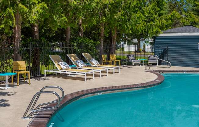 A pool surrounded by trees and chairs.
