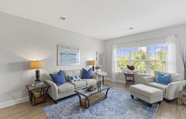 A living room with a grey couch, a blue rug, and a painting on the wall.