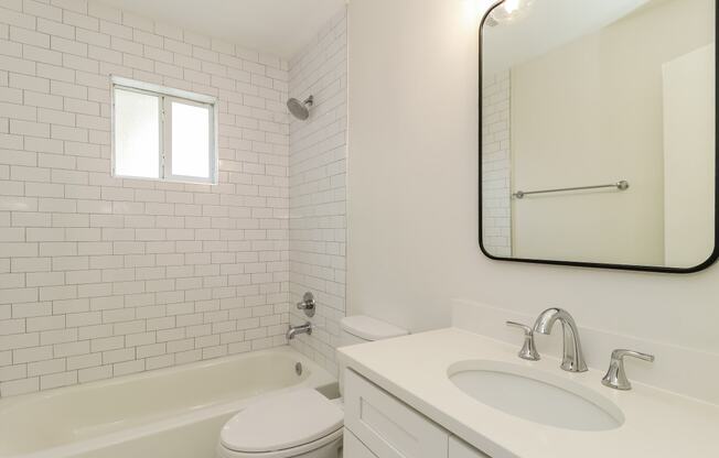 a bathroom with white tiles and a white sink and toilet