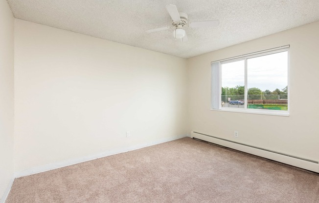 an empty bedroom with a ceiling fan and a window