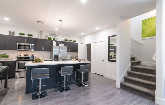 A kitchen with staircase and stools and island and ceiling lights and fridge and oven and microwave and stove