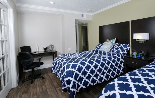 Fusion Orlando apartment bedroom with two full beds with blue and white duvets, espresso headboards, and modern lamp and night stand between.