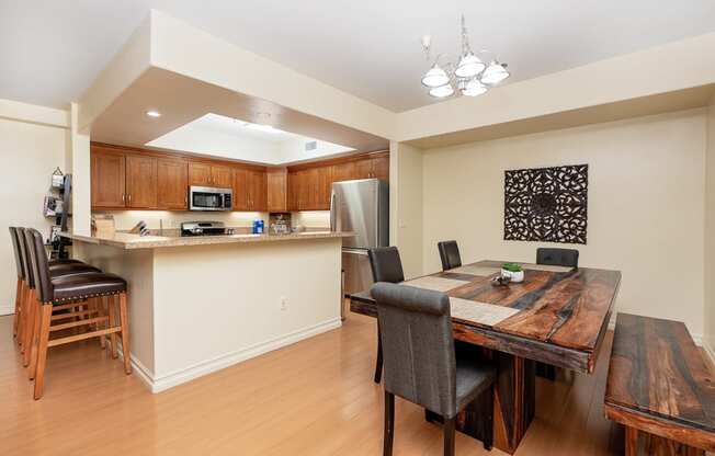 a dining area with a wooden table and chairs and a kitchen in the background