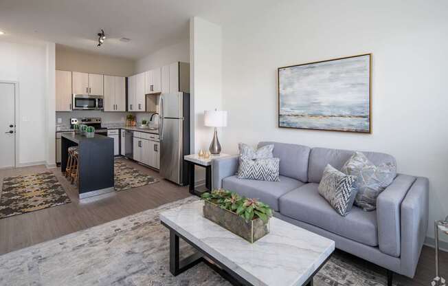A modern living room with a grey couch and a painting on the wall.