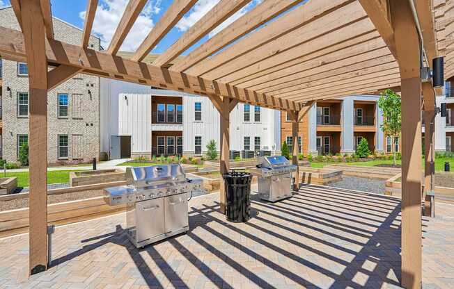 A wooden pergola over a patio with grills and trash can.