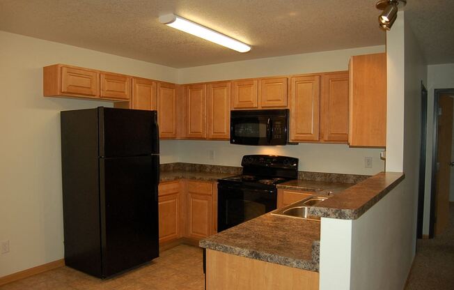 a kitchen with a black refrigerator freezer next to a stove top oven