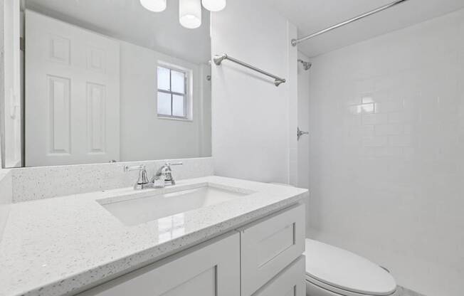 A white bathroom with a sink, toilet, and shower.