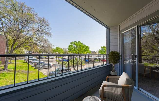 A balcony with a chair and a potted plant overlooking a parking lot.