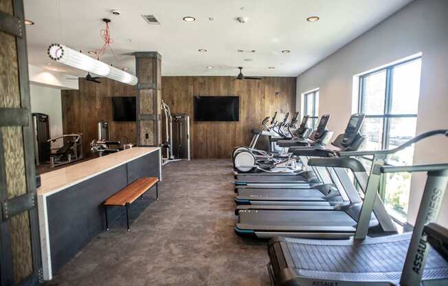 a gym with cardio machines and a counter with a tv