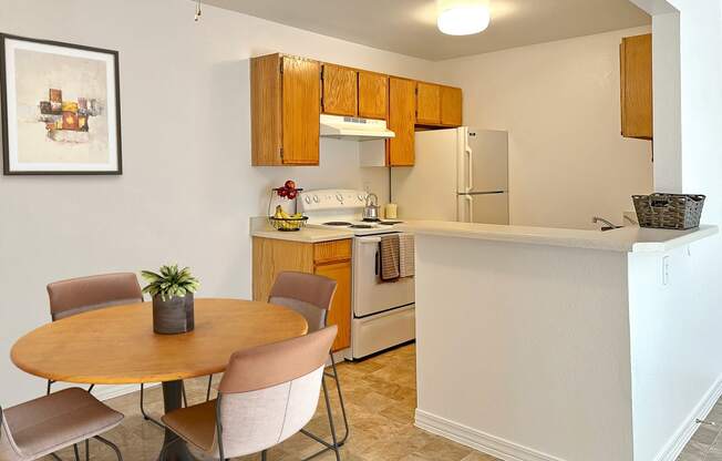 Bridgeside Landing Apartments in Taylorsville, Utah, Kitchen with wood cabinets, stove, fridge, dining area with round table and four chairs.