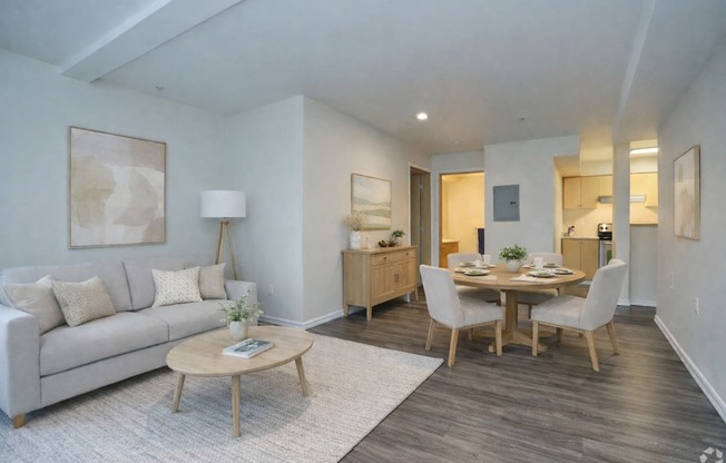 A living room with a grey couch, a wooden coffee table, and a dining table with chairs.