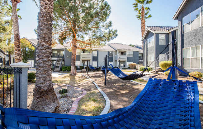 A blue hammock is in the foreground of a residential area with houses and palm trees.