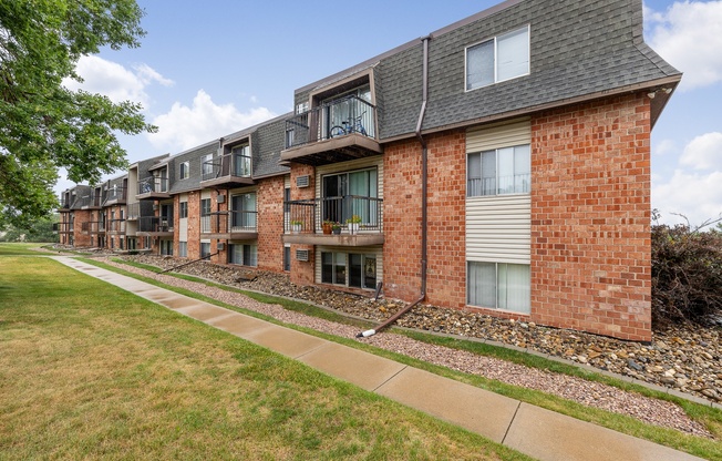 A row of red brick apartment buildings with a sidewalk in front.