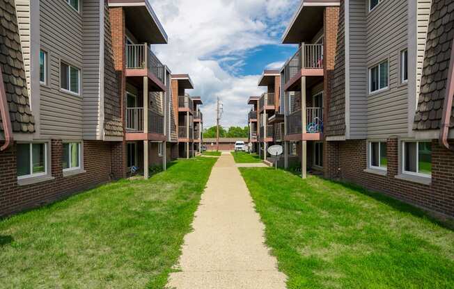 a walkway between two rows of buildings with grass on both sides