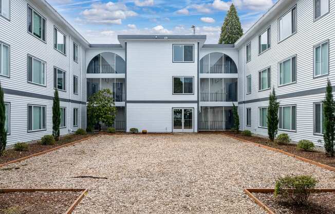 the courtyard of a white apartment building with a gravel area and trees