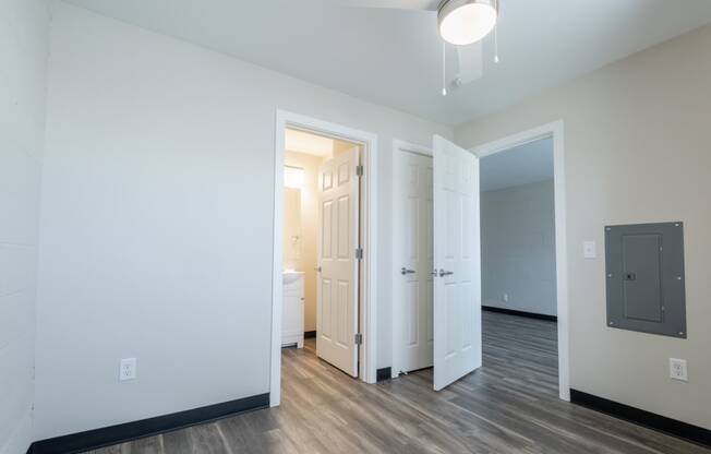 a living room with white walls and wood flooring and a door to a bathroom