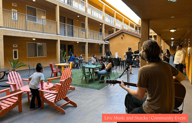 A man is playing a guitar at a live music and snacks community event.