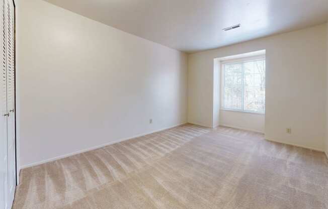 an empty bedroom with a large window and plush carpet