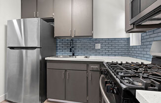 Blue tiled kitchen with stainless steel fridge, oven, and microwave.