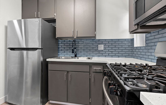 Blue tiled kitchen with stainless steel fridge, oven, and microwave.