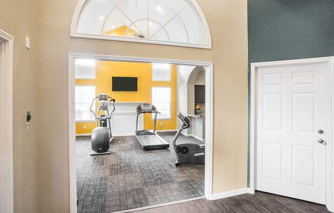 a gym with exercise machines and a yellow wall and a white door