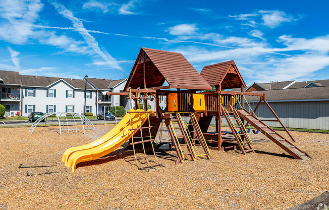 A playground with a yellow slide and a brown roofed structure.