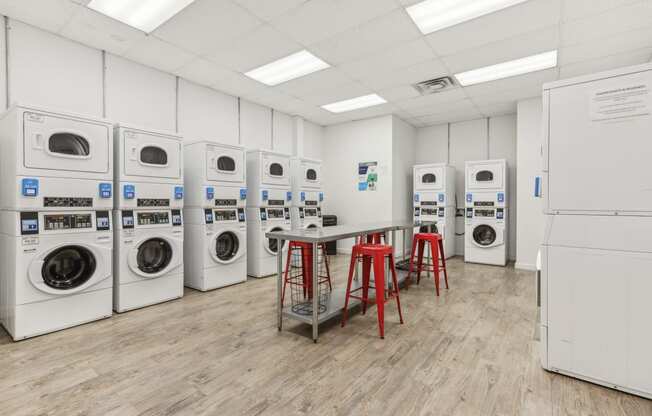 a laundry room with a row of washing machines and red stools