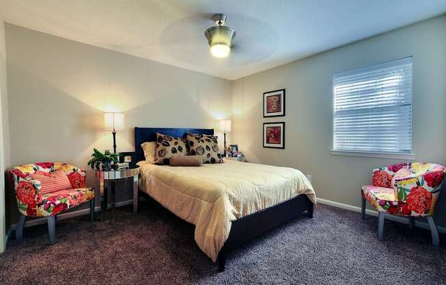 A bedroom with a bed, two chairs, and a nightstand.