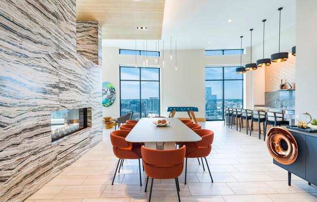 Community lounge with a shared table, fireplace, and bar seating framed by expansive windows and warm architectural details.