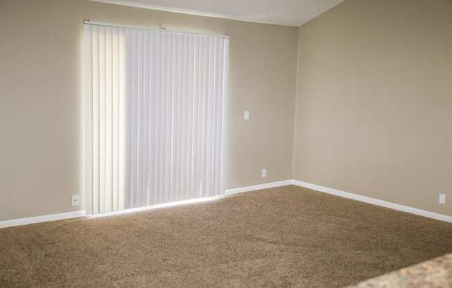 an empty living room with a large window with white blinds. Omaha, NE Evergreen Terrace Apartments