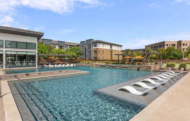 A large swimming pool with lounge chairs is surrounded by buildings.