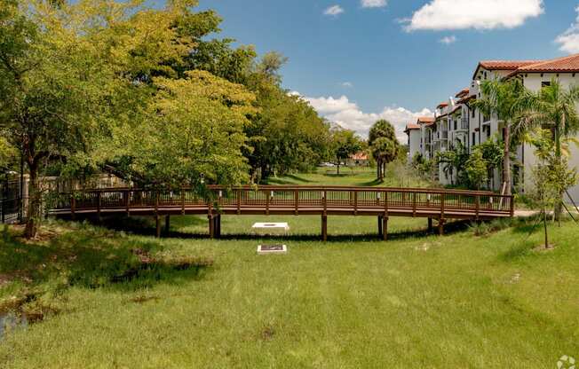 a bridge over a grassy area with trees and buildings in the background