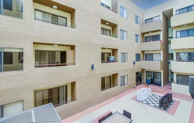 A courtyard with a chess board and chess pieces in the middle of a courtyard surrounded by buildings.