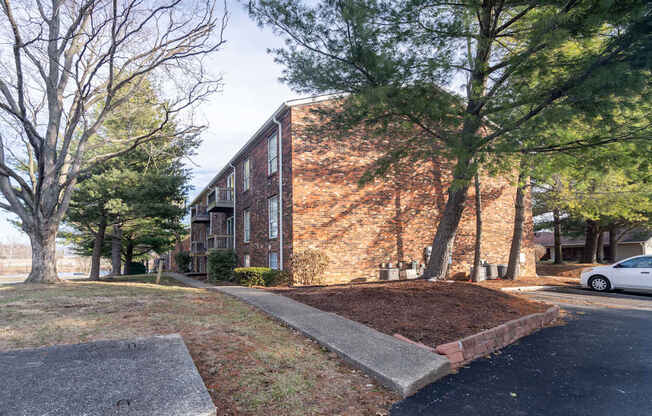 A white car is parked on the street in front of a brick building.