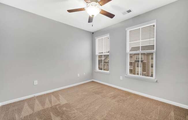 an empty living room with a ceiling fan and two windows