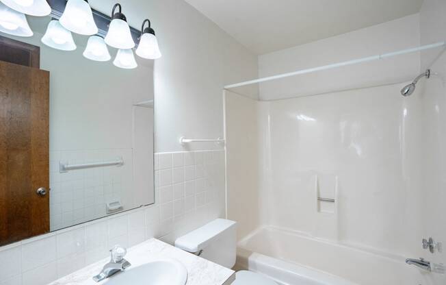 a white bathroom with a tub and a sink and a mirror. Fargo, ND Betty Ann Apartments