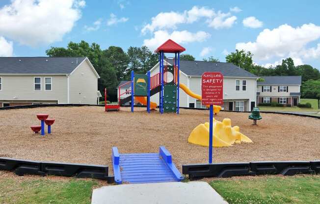 a playground with a slide and monkey bars in a park with houses in the background