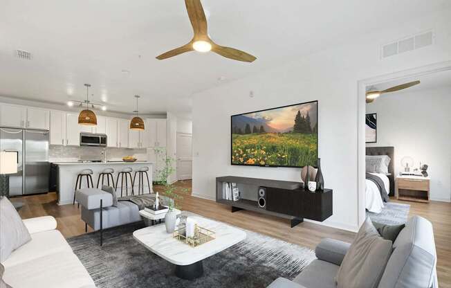 A modern living room with a grey sofa set, a coffee table, a ceiling fan, and a large painting on the wall.