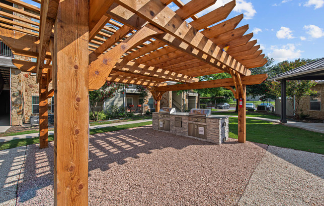 a covered patio with a stone grill and a wooden structure