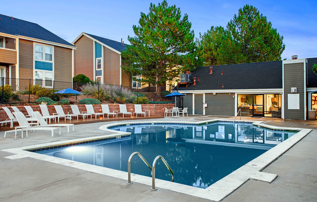 A swimming pool surrounded by lounge chairs and umbrellas in a residential area.