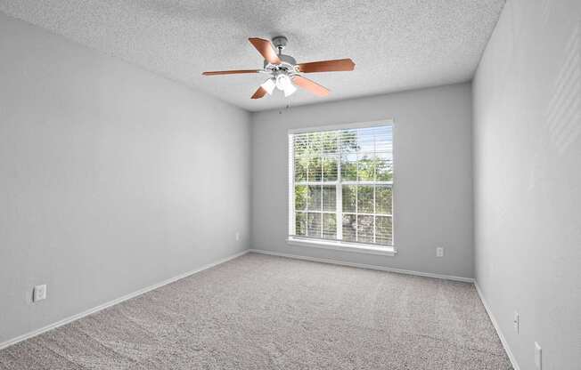 A room with a ceiling fan and a window overlooking a fence.