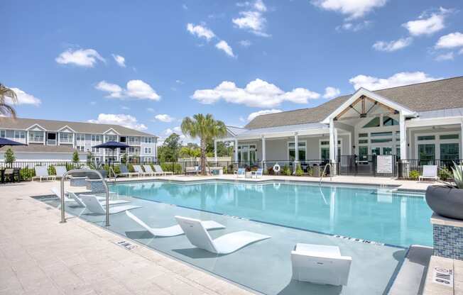 a swimming pool with white chairs and a building in the background