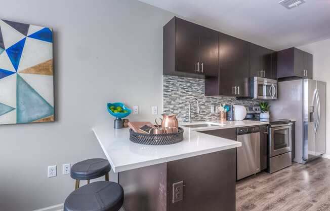 a kitchen with dark cabinets and a white counter top with two stools in front of it